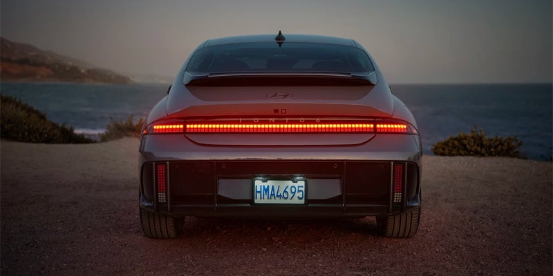 Rear view of modern electric sedan with LED tail light bar at sunset near water
