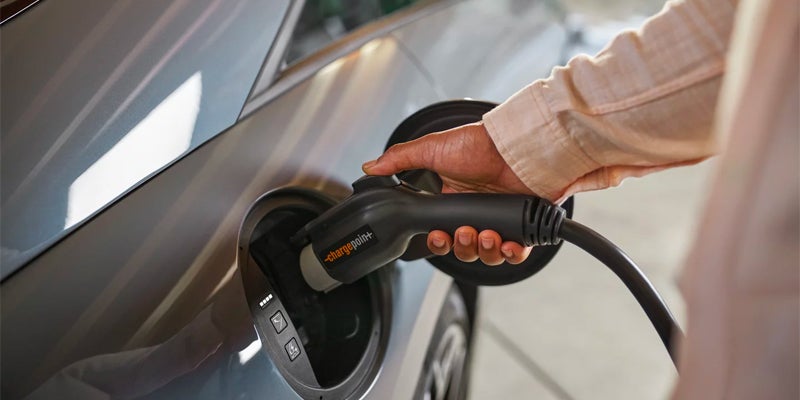 Close-up of electric car charging port with hand plugging in charger