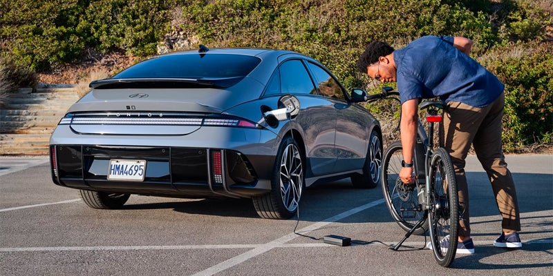 Electric sedan parked while a bicycle is being loaded on rear rack