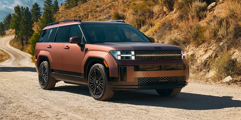 Front-side view of copper SUV parked near rocky terrain under sunlight