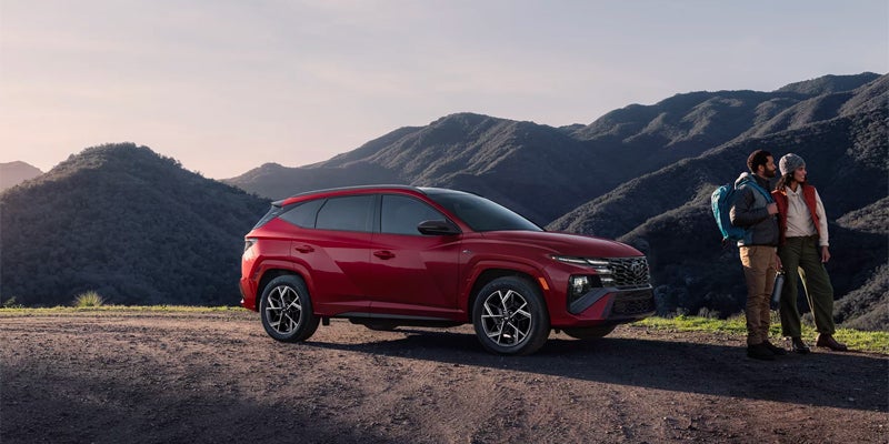 A red SUV parked on a dirt road, with two hikers and mountains in the background at sunset