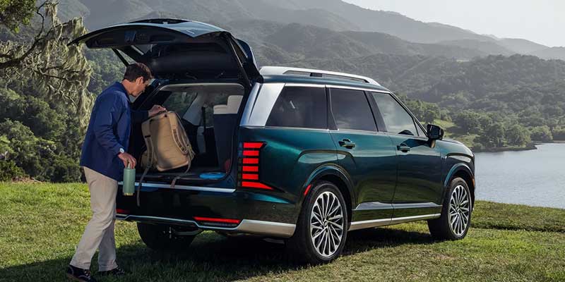 Rear three-quarter view of a dark green SUV parked on grass near a lake or reservoir