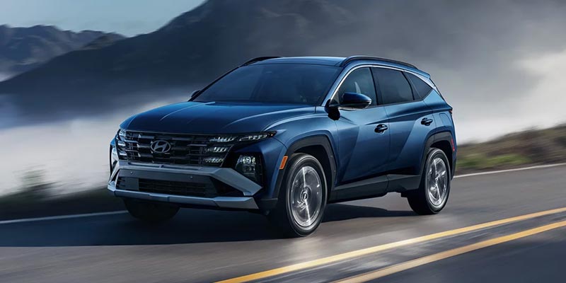 A blue Hyundai Tucson is driving on a paved road