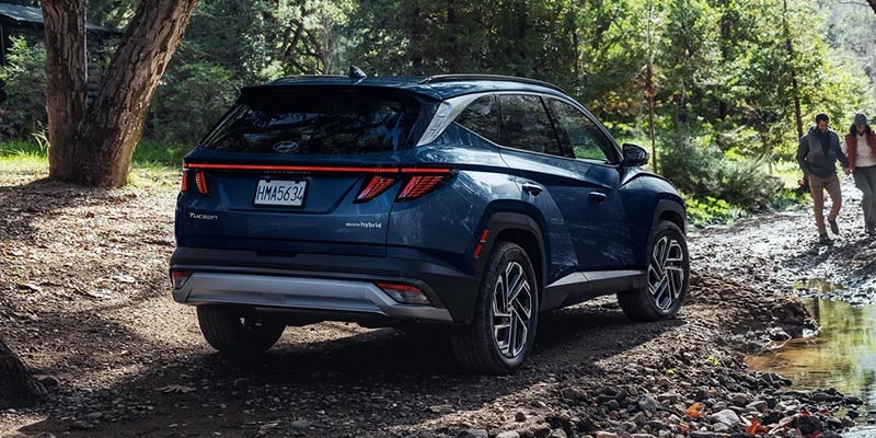 A Hyundai Tucson Hybrid parked on a wooded trail, surrounded by trees and natural scenery.