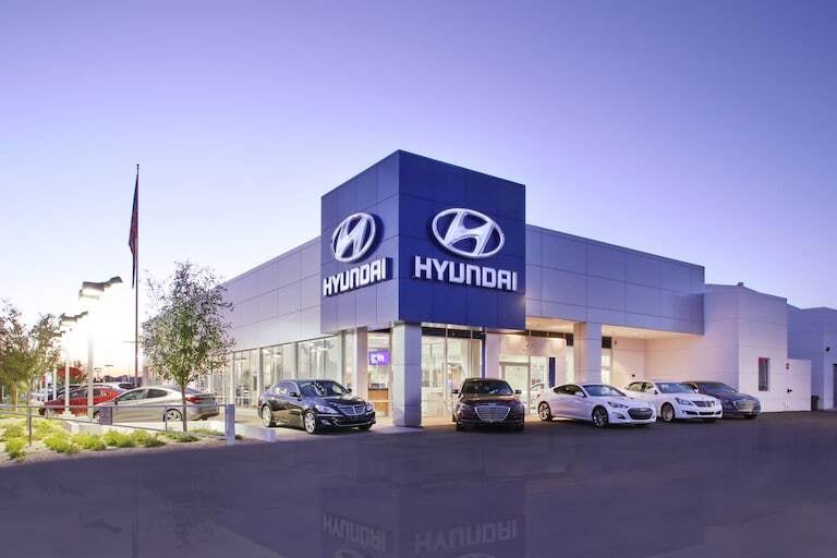 A modern Hyundai automotive dealership with large glass windows and glowing blue branding, cars parked outside