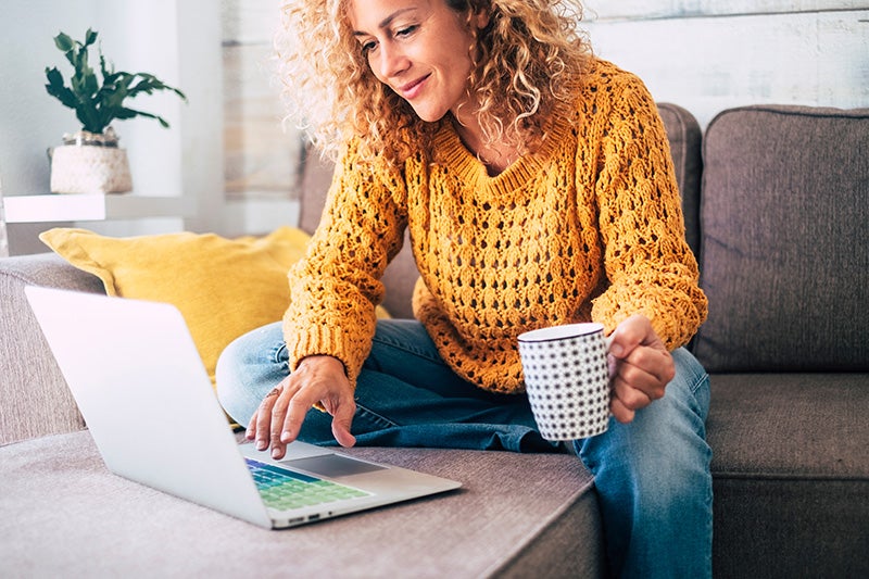 The person is working or interacting with a silver-colored laptop placed on a matching upholstered ottoman or coffee table