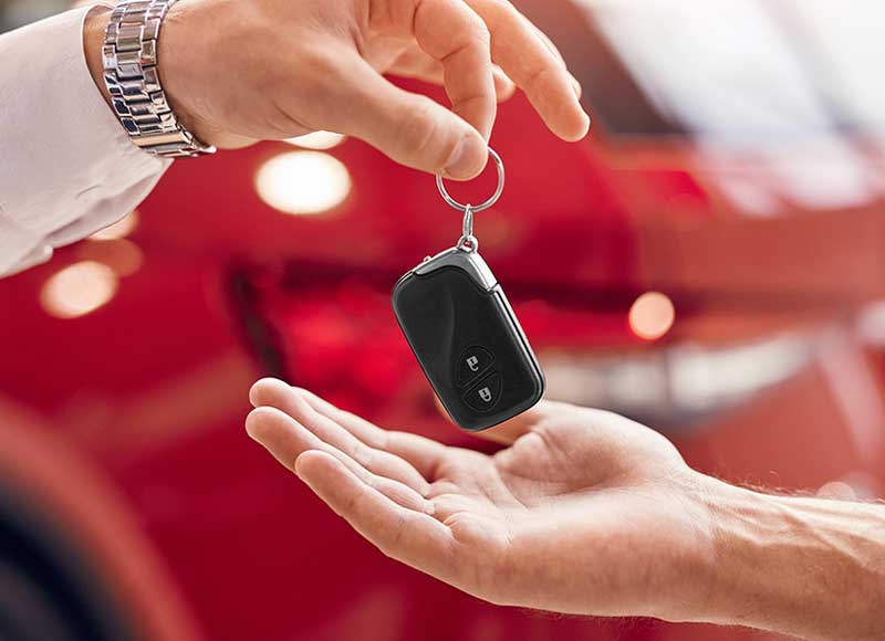 Vehicle key fob being handed from one person to another in front of a red car